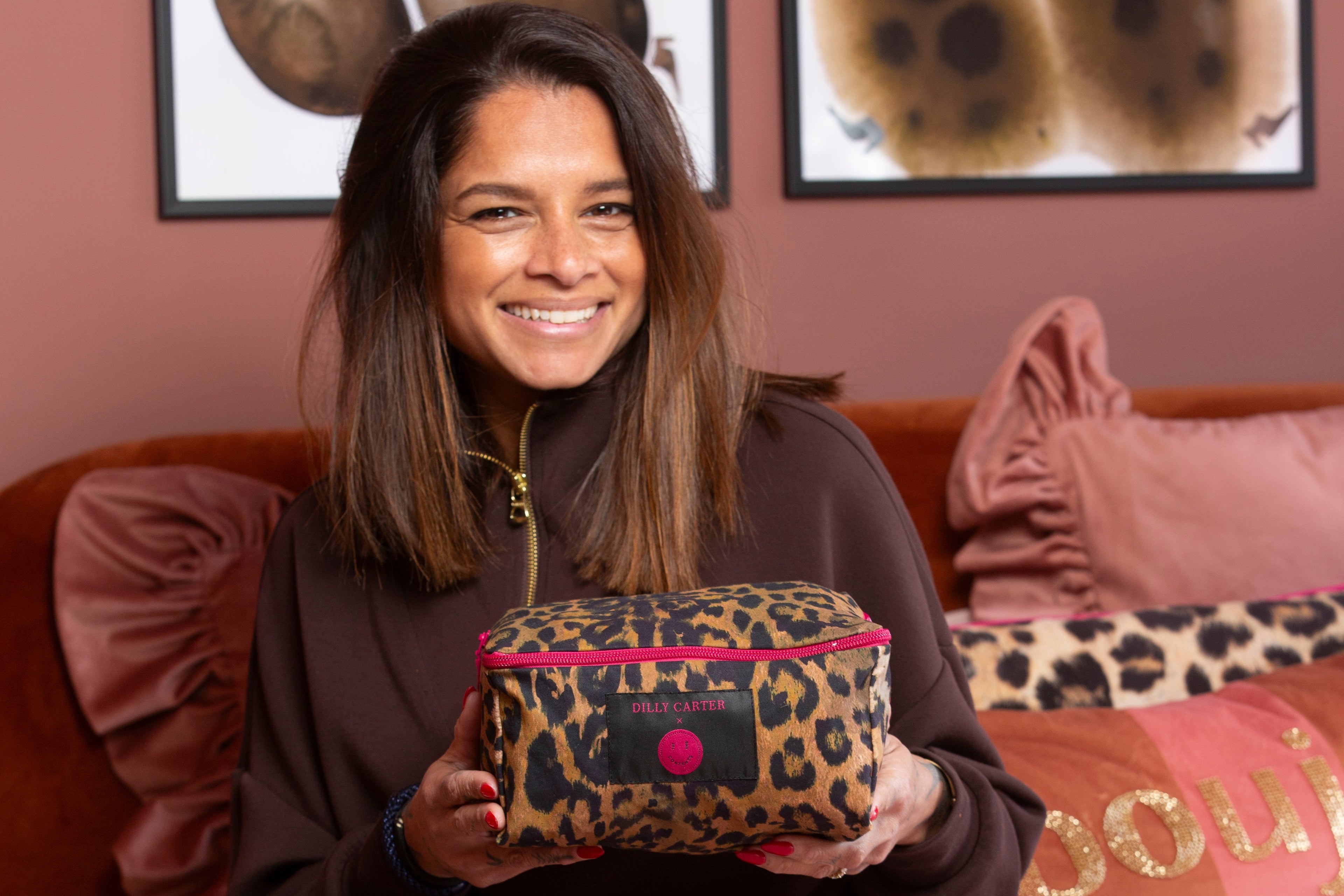 Woman sitting on a couch holding a leopard print packing cube with a pink interior, smiling.