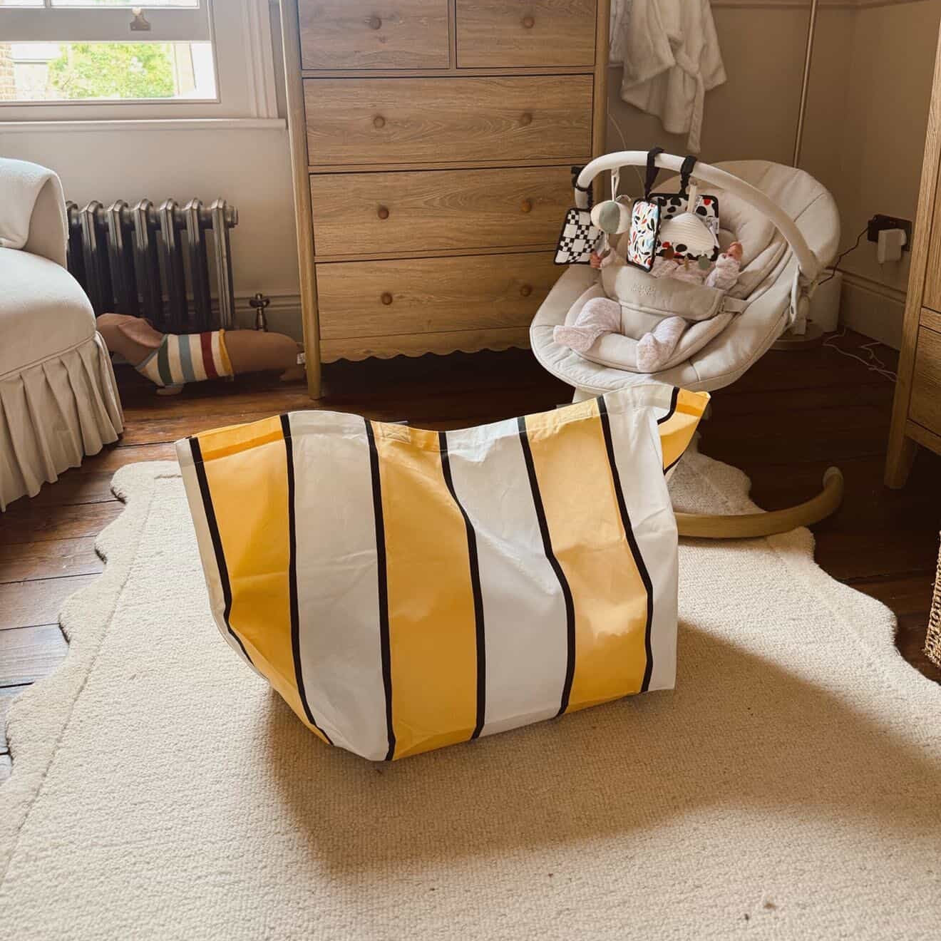 Nursery room with wooden dresser, baby swing, and yellow striped bag.